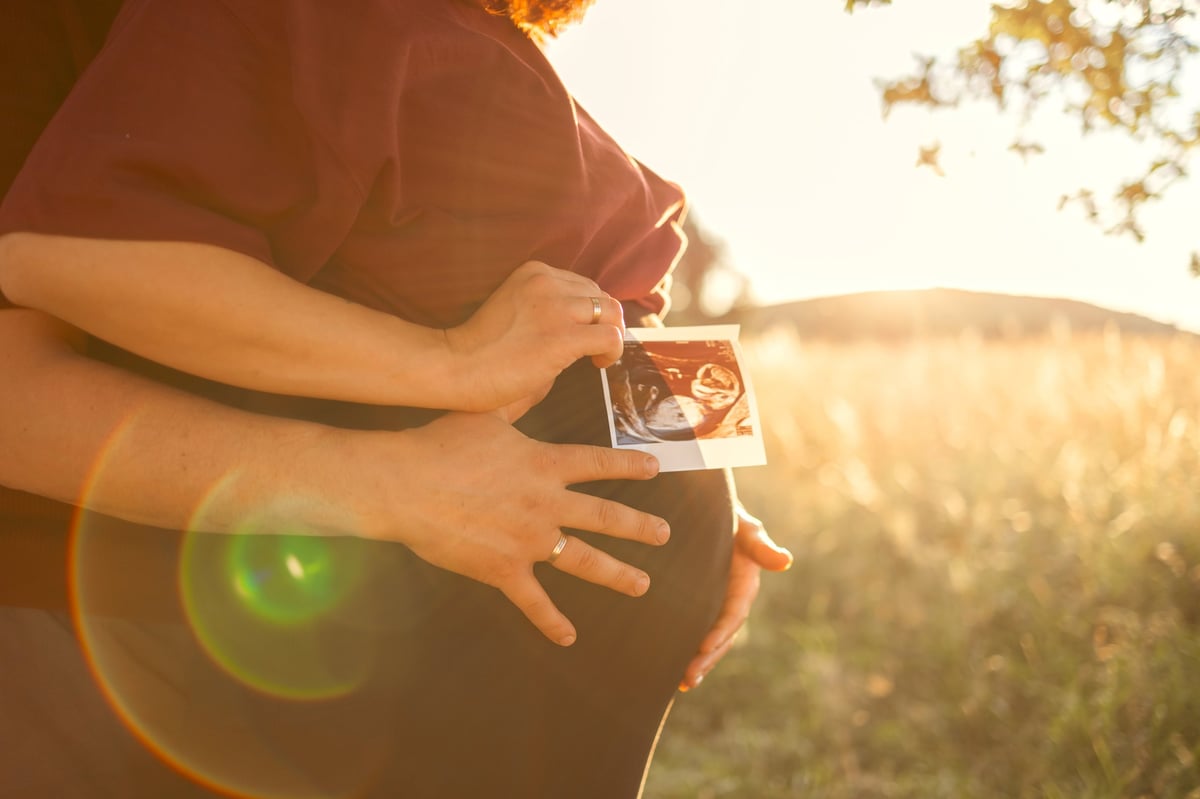 close-up of a pregnant woman's belly with parents holding an ultrasound photo of their baby