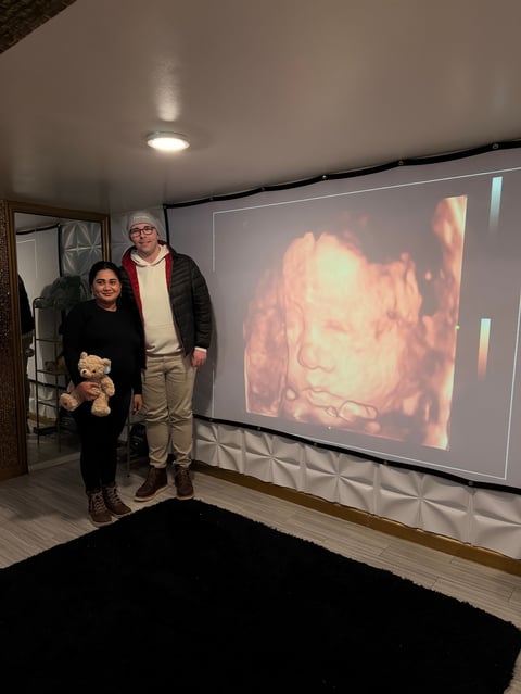 Two people standing in a home theater room next to a large projection screen displaying a close-up portrait image